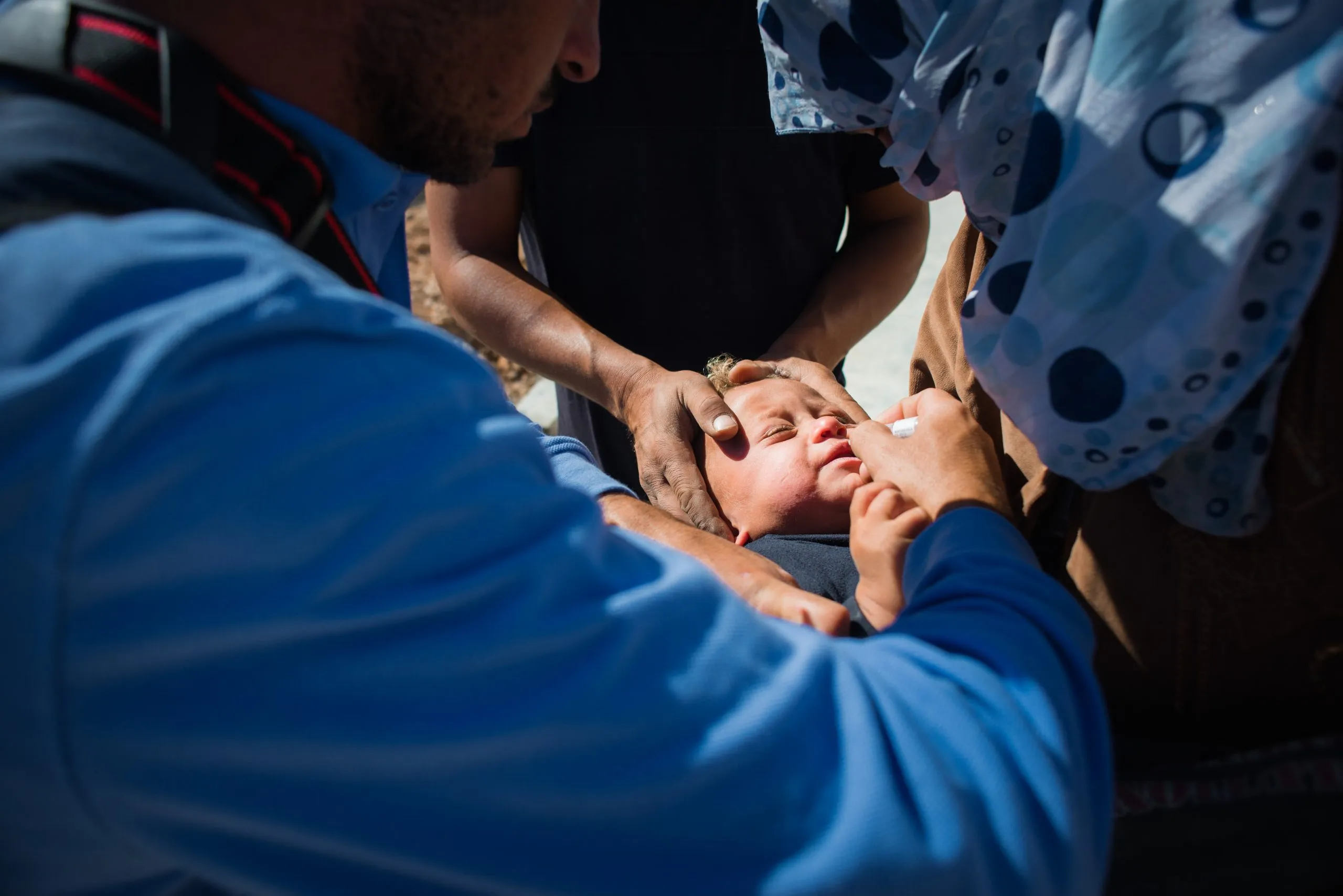 A health worker administers oral polio vaccine drops to a baby held by a parent during a vaccination drive in Jordan.